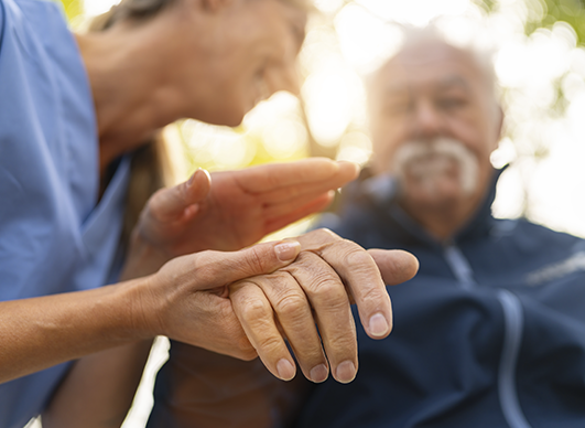 Cuidadora segurando a mão de um idoso enquanto conversa com ele, transmitindo um momento de carinho e atenção.
